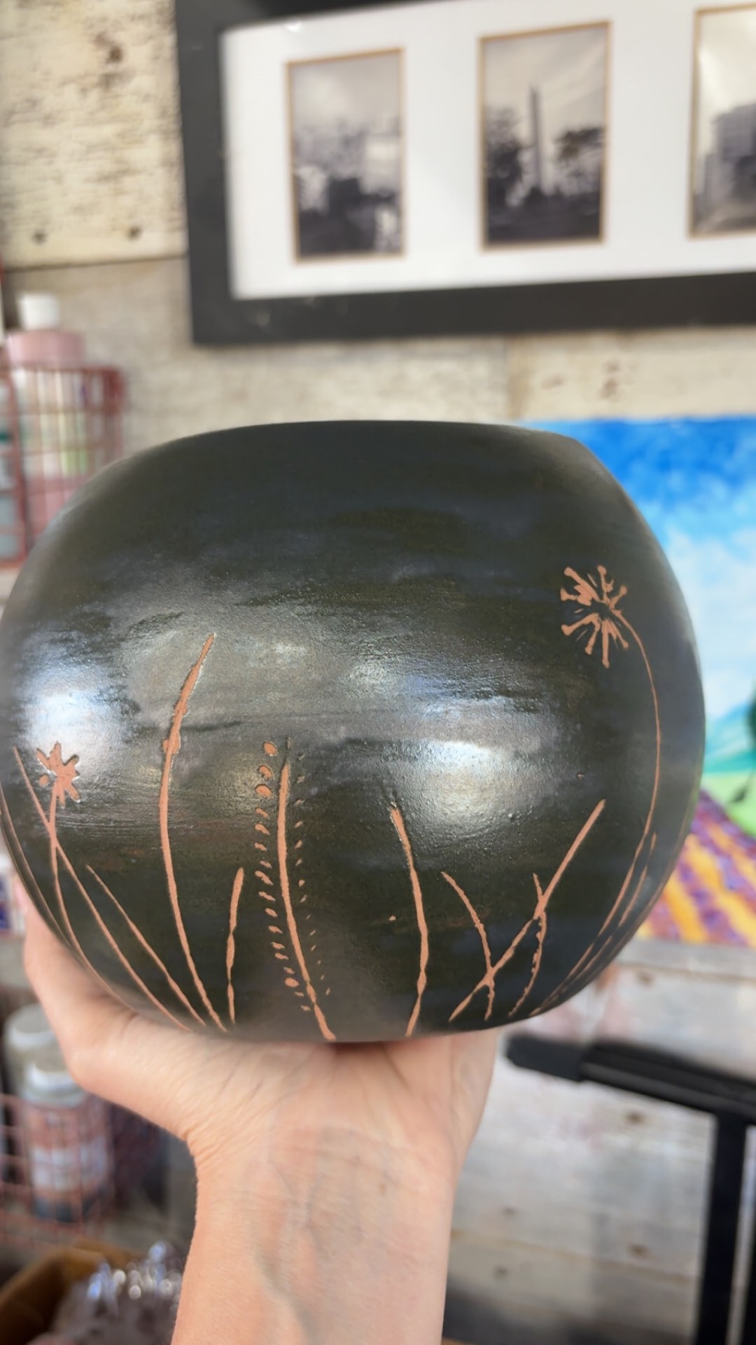 Dark round ceramic vessel with copper-colored incised grasses